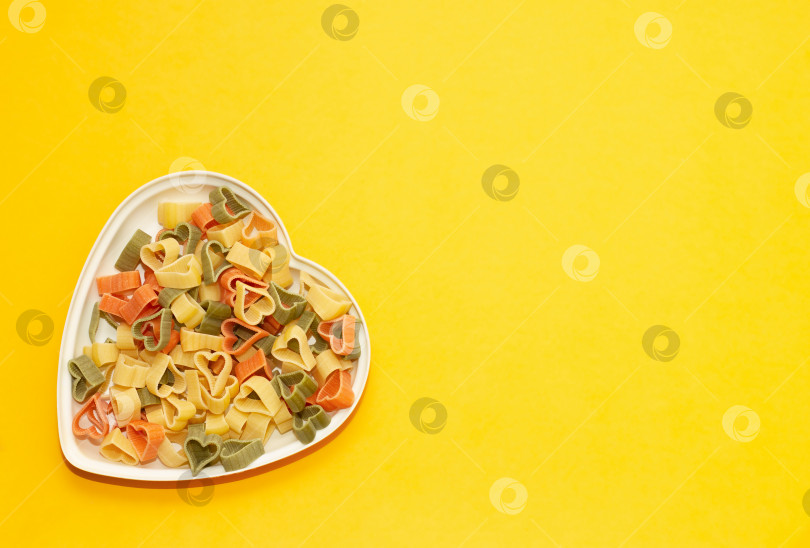 Скачать тарелка в форме сердца, наполненная цветной пастой на желтом фоне с помощью вилки. концепция питания. правильное питание. фотосток Ozero