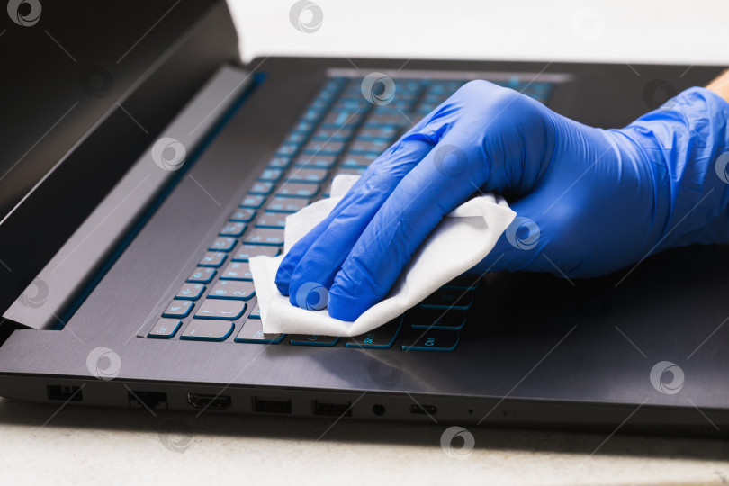 Скачать Мужская рука в перчатке чистит клавиатуру ноутбука антибактериальным средством для защиты от эпидемии covid-19. Очистка поверхности от бактерий спиртовой салфеткой фотосток Ozero