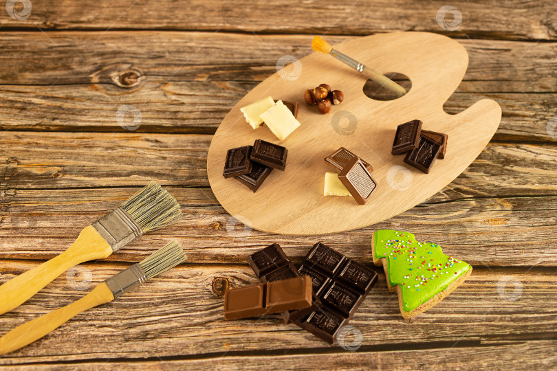 Скачать Шоколадное ассорти оформлено в художественной палитре на теплом деревянном фоне. фотосток Ozero