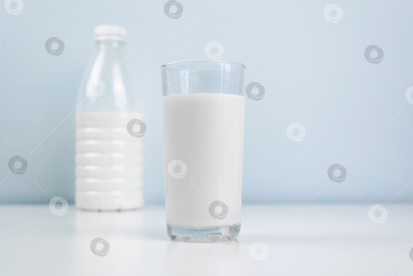 Скачать Стакан молока и бутылка стоят на белом столе в помещении. Концепция утреннего здорового завтрака. Минималистичная фотография. фотосток Ozero