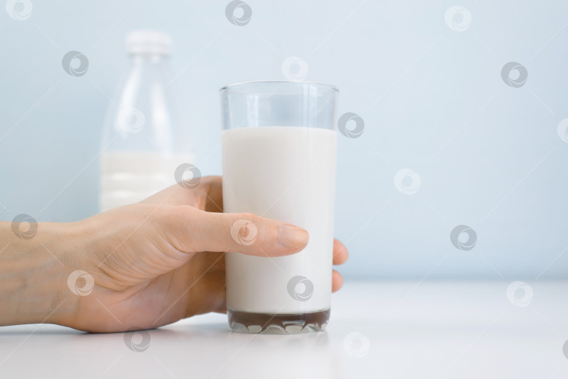Скачать Рука, держащая стакан молока на белом столе в помещении, крупным планом. Утренний завтрак, здоровое питание, концепция диеты. фотосток Ozero