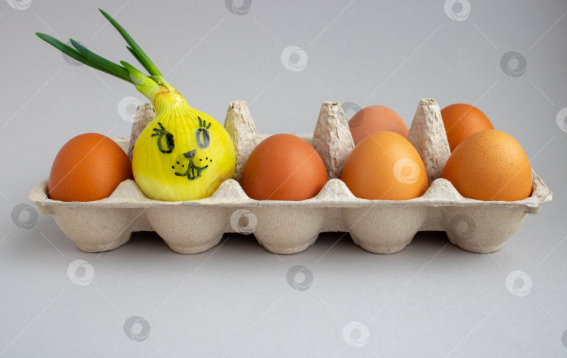 Скачать пророщенный лук выложите на решетку с коричневыми яйцами. на луке нарисована мордочка кролика.Концепция Пасхи фотосток Ozero