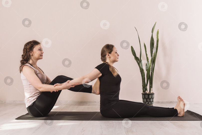 Скачать Учитель йоги выполняет вытяжение позвоночника ученика, сидящего на коврике в студии у стены, - техника для улучшения осанки фотосток Ozero