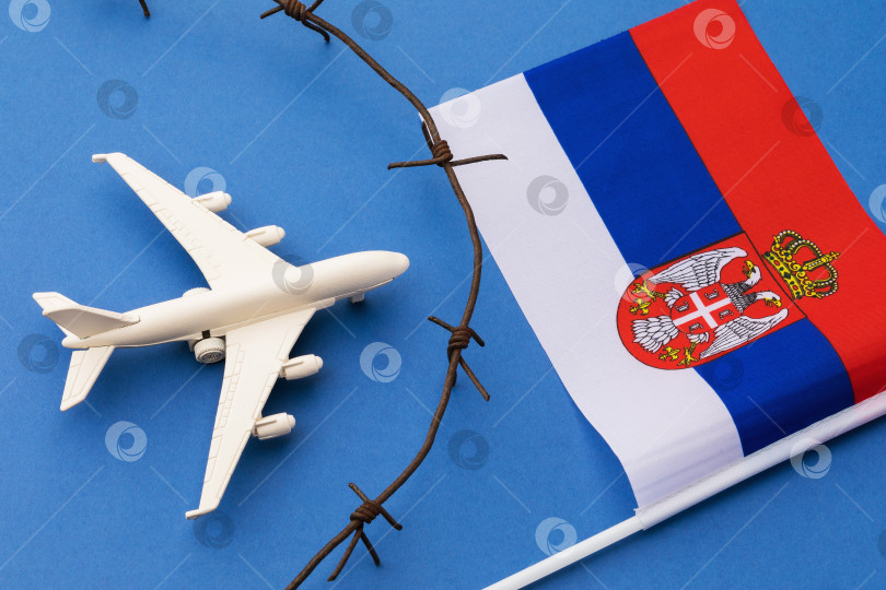 Скачать Игрушечный самолет, флаг и колючая проволока на синем фоне, концепция закрытой воздушной границы Сербии фотосток Ozero
