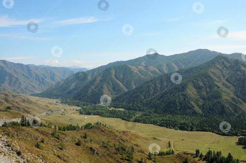 Скачать Извилистая дорога солнечным летним днем спускается по пологому склону в живописную долину, окруженную высокими горами. фотосток Ozero