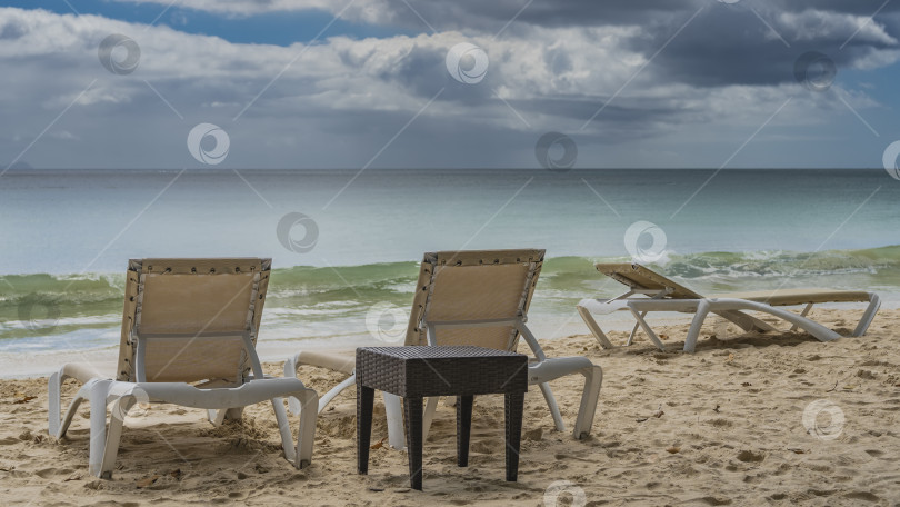 Скачать На песчаном пляже установлены шезлонги и плетеный столик. фотосток Ozero