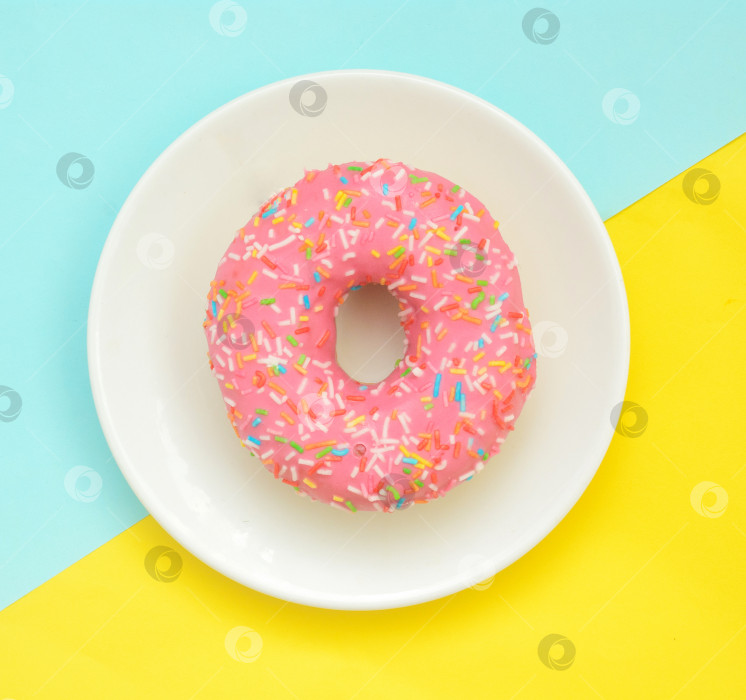 Скачать Пончик в розовой глазури на белой тарелке на пастельно-желто-бирюзовом фоне фотосток Ozero