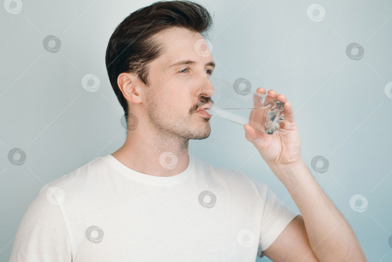 Скачать Молодой человек пьет воду из стакана в помещении, крупным планом. Красивый усатый парень и стакан воды на светлом фоне фотосток Ozero