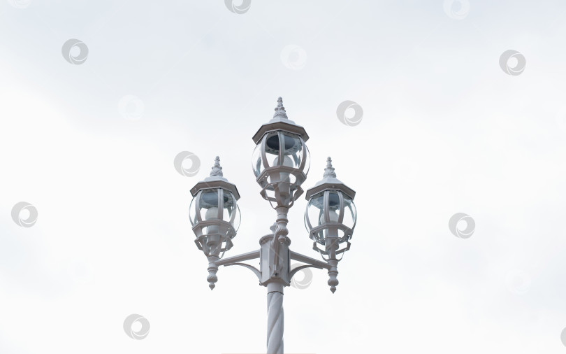 Скачать Старинный уличный фонарь на фоне яркого неба в течение дня. Три лампы на декоративном столбе. фотосток Ozero