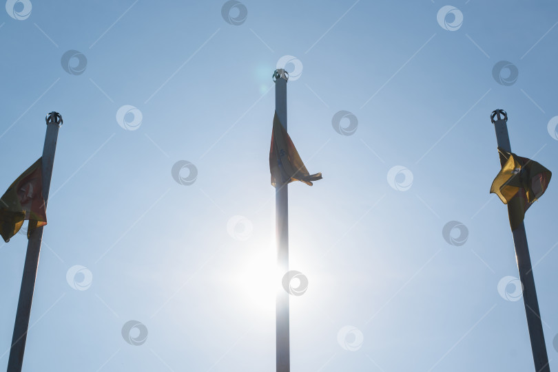 Скачать Три флагштока с флагами на фоне солнечного голубого неба, вид снизу. Концептуальная встреча, конференция, саммит фотосток Ozero