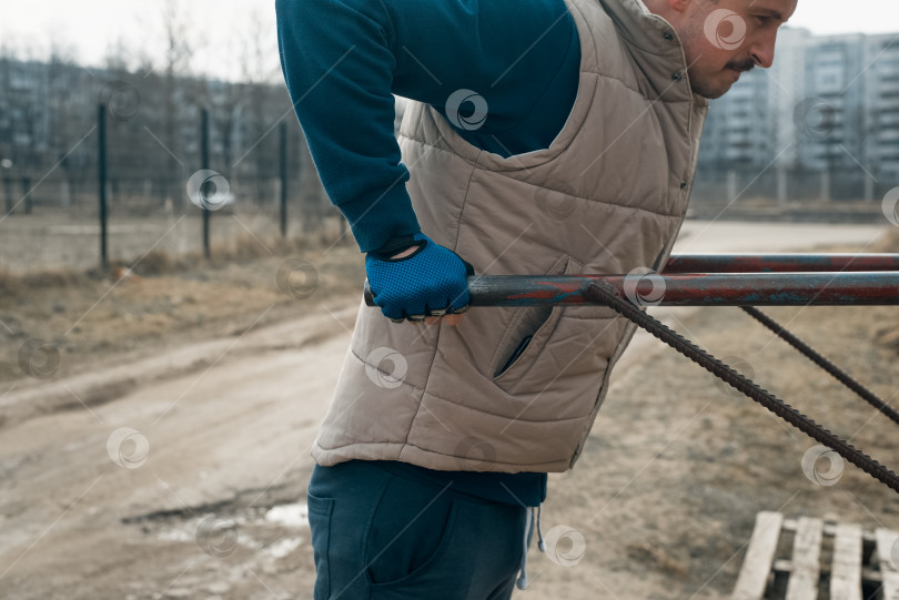 Скачать Молодой человек в спортивных перчатках тренируется на брусьях снаружи. Обрезка. Силовая тренировка на открытом воздухе фотосток Ozero