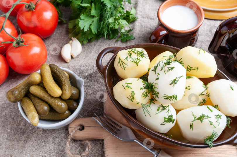 Скачать Отварной картофель с зеленью в глиняном горшочке. Рядом в белой чашке фотосток Ozero