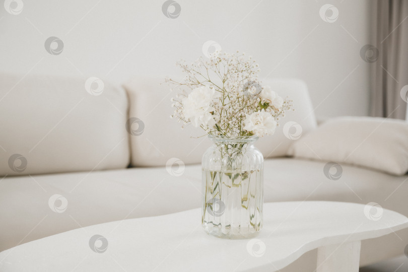 Скачать Ваза с белыми нежными цветами на столешнице на размытом фоне современной гостиной фотосток Ozero