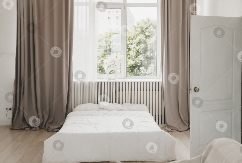 Скачать Интерьер белой спальни с занавесками и белыми подушками на деревянной кровати - классика для отдыха и сна. Современная белая спальня очень светлая. фотосток Ozero