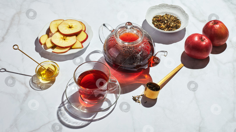 Скачать Фруктовый чай с яблоками, тимьяном и медом в стеклянном чайнике и чашке на белом фоне с резкими тенями фотосток Ozero