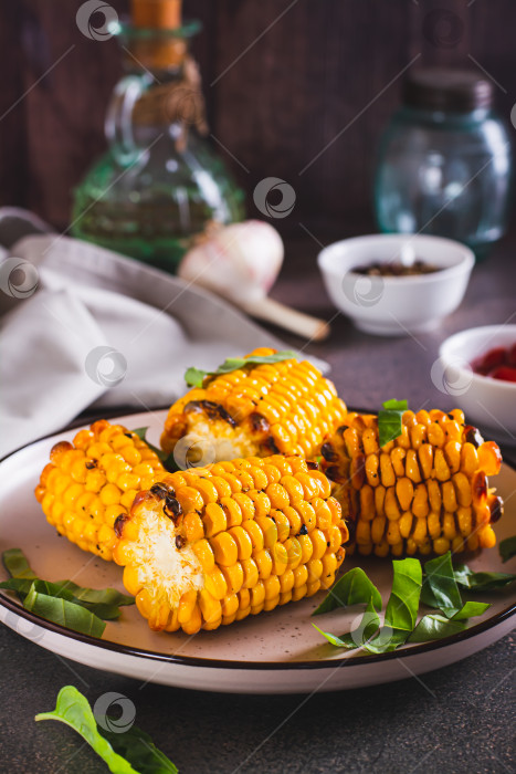 Скачать Запеченные початки сладкой кукурузы со сливочным маслом, чесноком и зеленью на тарелке v фотосток Ozero