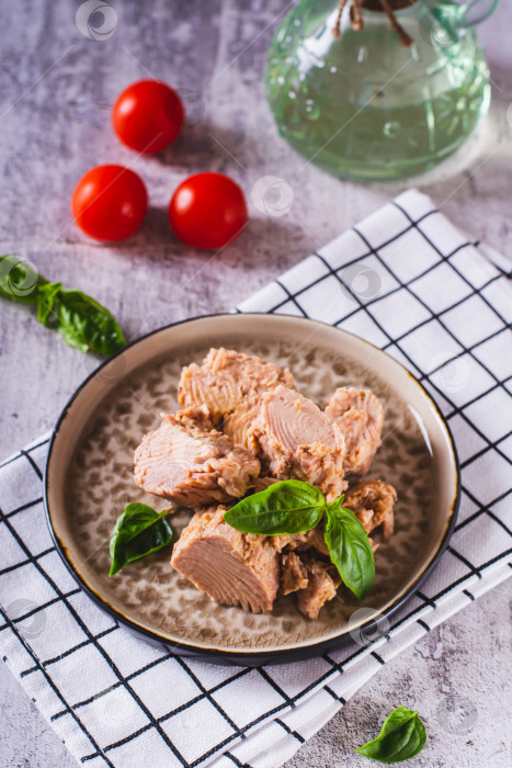 Скачать Консервированный тунец с мясом и базиликом на тарелке, стоящей вертикально на столе фотосток Ozero