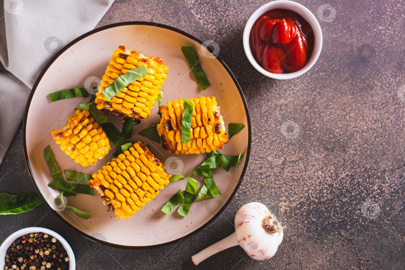 Скачать Запеченные початки сладкой кукурузы со сливочным маслом, чесноком и зеленью на тарелке фотосток Ozero