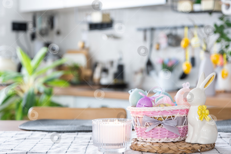Скачать Пасхальное украшение из разноцветных яиц в корзинке и кролика на кухонном столе в деревенском стиле. Праздничный интерьер загородного дома фотосток Ozero