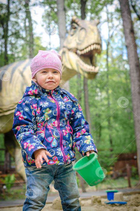 Скачать Девушка с совком и ведром в руках. На заднем плане изображен огромный динозавр. фотосток Ozero