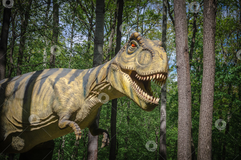 Скачать Ульяновск, Россия - 08 мая 2023 года: Динозавр в сосновом лесу. Реалистичный манекен динозавра в парке развлечений фотосток Ozero