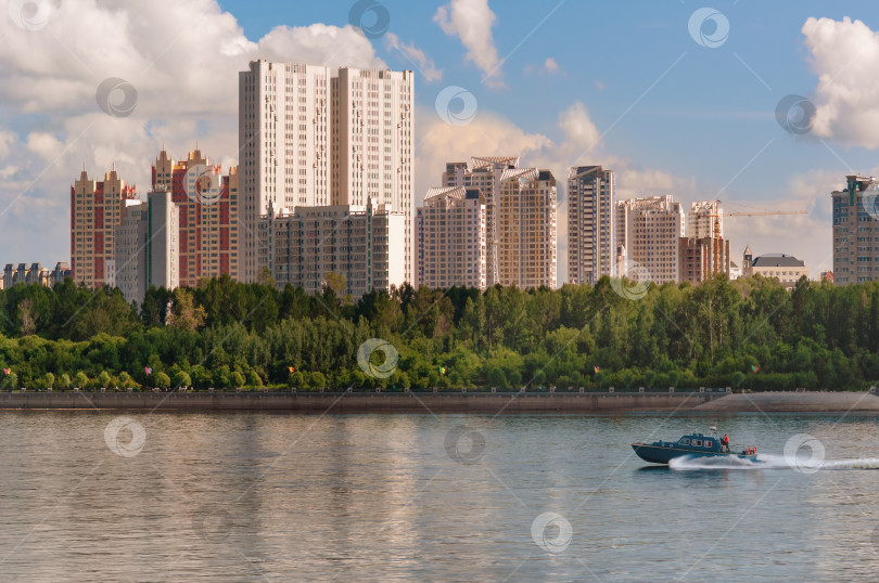 Скачать Здания жилого городского района на лесистом берегу. Быстроходный катер мчится по водной глади реки. фотосток Ozero