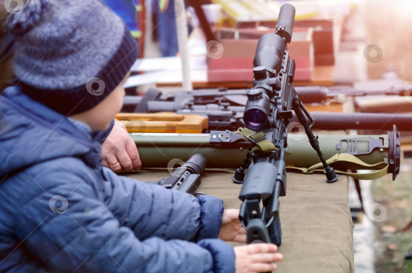 Скачать Снайперскую винтовку и гранатомет осматривает мальчик 8-10 лет. фотосток Ozero