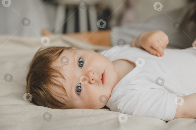 Скачать Очаровательная голубоглазая 6-месячная малышка лежит в кроватке в белом боди. Вид сверху фотосток Ozero