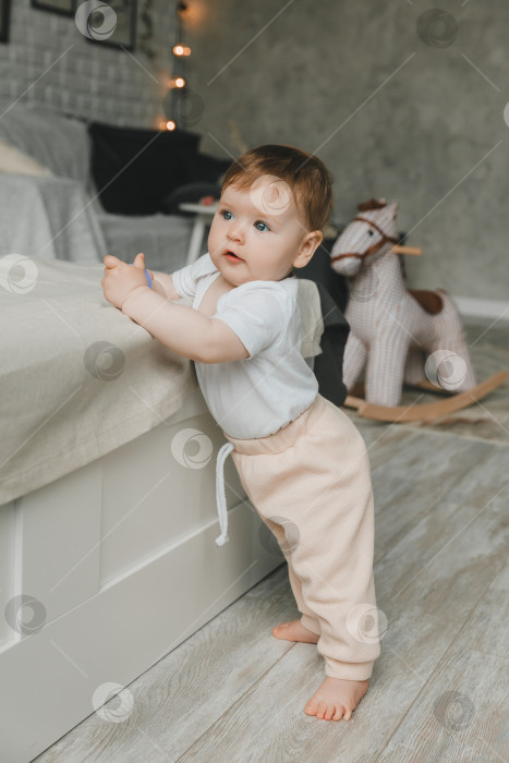 Скачать Возле кровати стоит симпатичный маленький ребенок в возрасте 6-9 месяцев. фотосток Ozero