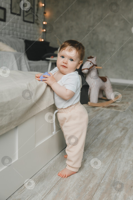 Скачать Возле кровати стоит симпатичный маленький ребенок в возрасте 6-9 месяцев. фотосток Ozero
