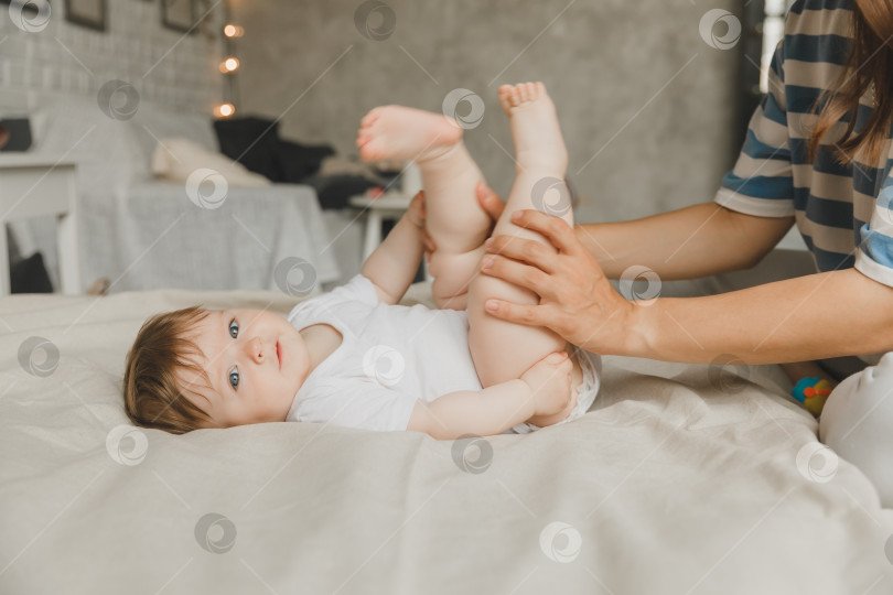 Скачать Мама делает массаж стоп 6-месячному малышу дома на кровати. мать играет с ребенком дома. фотосток Ozero