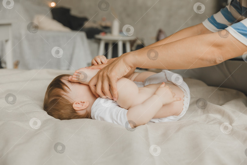 Скачать Мама делает массаж стоп 6-месячному малышу дома на кровати. мать играет с ребенком дома. фотосток Ozero