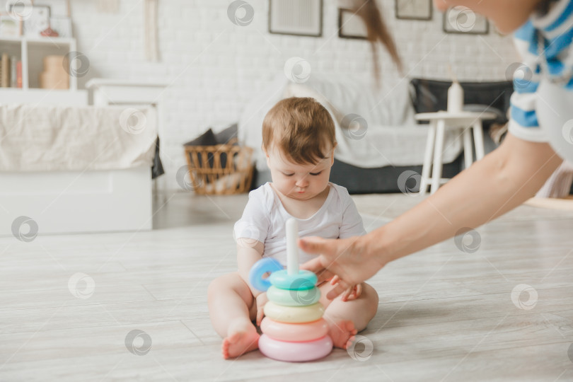 Скачать Красивая молодая мама играет и учит своего 6-месячного ребенка на полу в гостиной. мама и малыш играют с игрушками фотосток Ozero