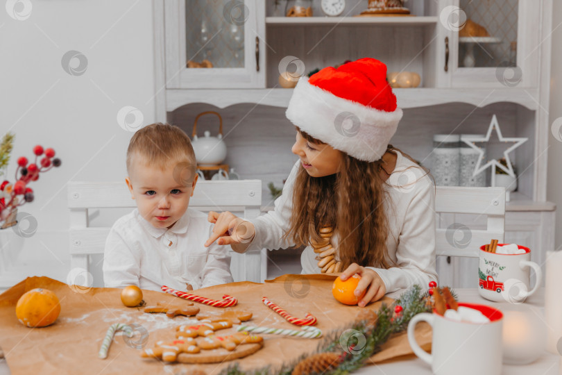 Скачать маленькие дети, брат и сестра в рождественской шапочке, готовят печенье на кухне у себя дома фотосток Ozero