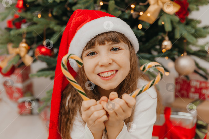 Скачать Счастливая девочка-ребенок держит в руках рождественские леденцы. Счастливая маленькая девочка счастлива в канун Рождества. Полное надежд дитя. канун Нового года. фотосток Ozero