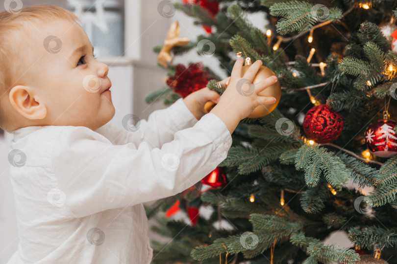 Скачать Ребенок украшает рождественскую елку дома. Маленький мальчик в белой рубашке. Рождество. фотосток Ozero