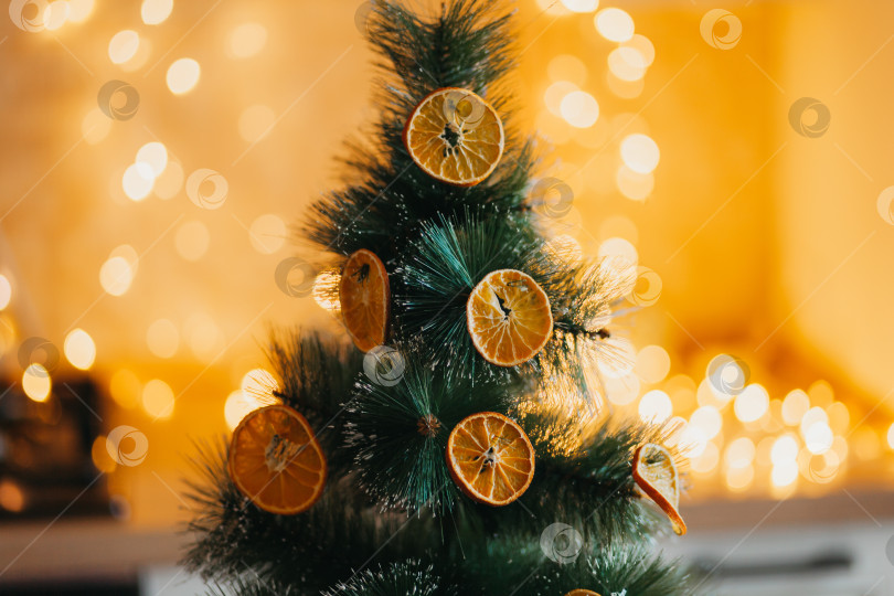 Скачать Зимой елку снаружи украшают сушеными апельсинами, зелеными ветками на размытом фоне и желто-золотым боке. Праздничный декор в эко-стиле. счастливого Рождества. фотосток Ozero