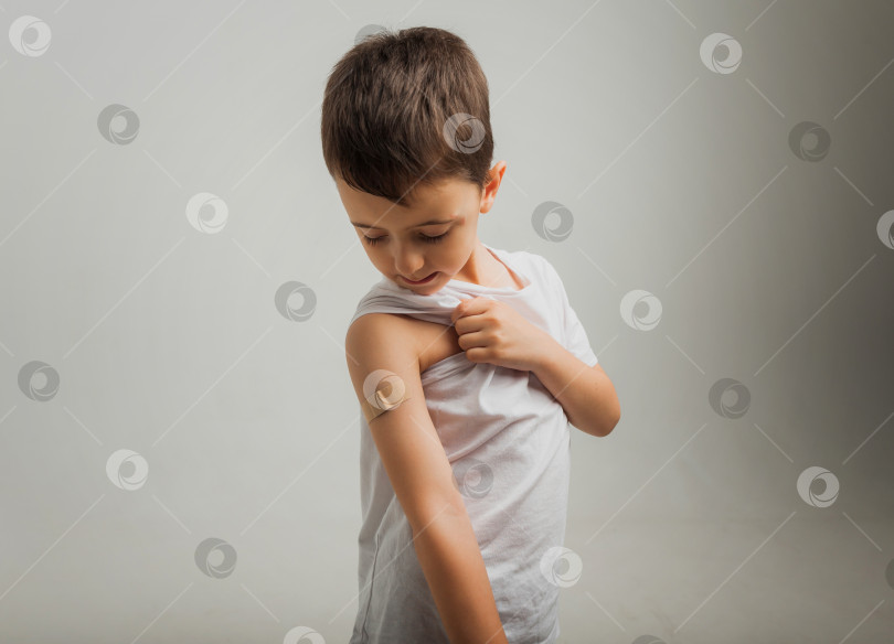 Скачать Улыбающийся мальчик показывает пластырь на своей руке. Концепция вакцины. мальчику была сделана прививка в руку. фотосток Ozero