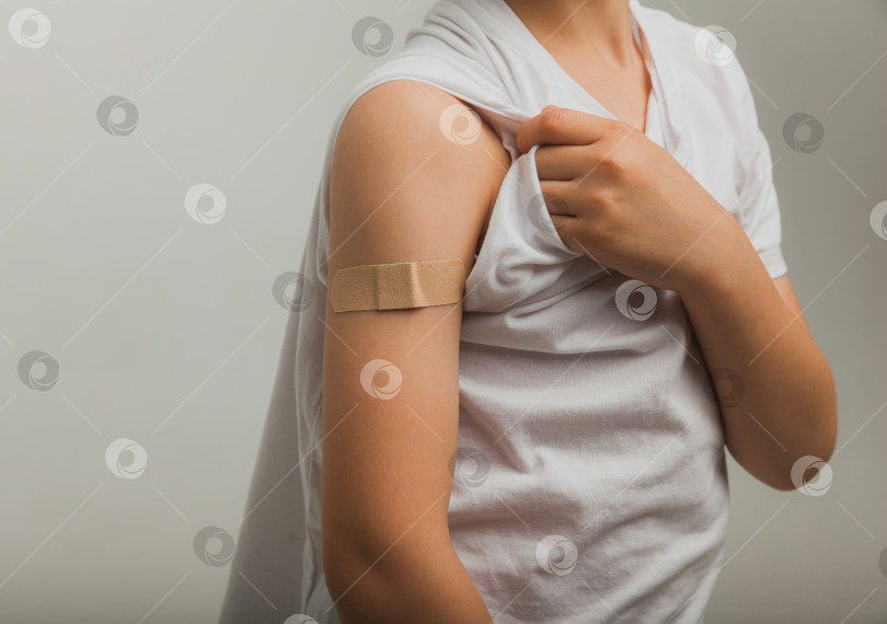 Скачать Улыбающийся мальчик показывает пластырь на своей руке. Концепция вакцины. мальчику была сделана прививка в руку. фотосток Ozero