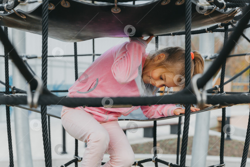 Скачать Счастливая девочка-подросток, играющая в веревочной паутине на детской площадке. детский спорт. фотосток Ozero
