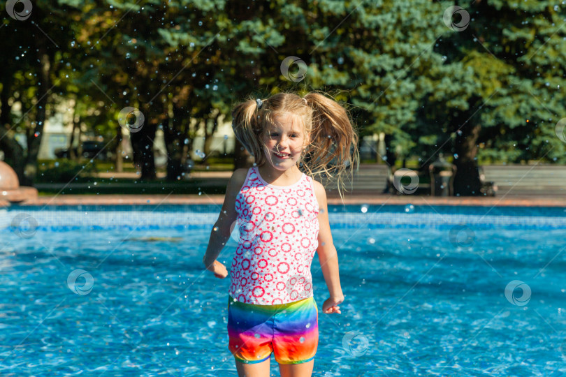 Скачать Милая жизнерадостная маленькая девочка играет в фонтане. Ребенок веселится в летнем парке у городского фонтана. фотосток Ozero