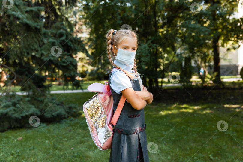 Скачать маленькая школьница в медицинской маске сидит в парке на траве и развлекается. фотосток Ozero