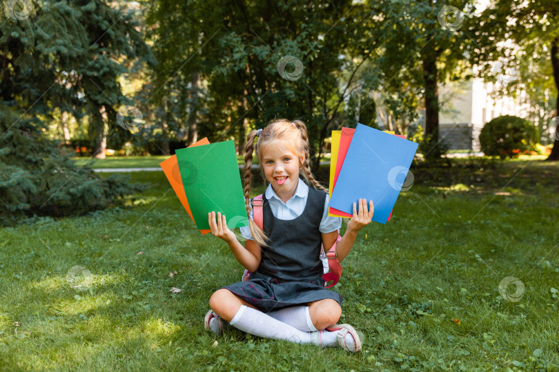 Скачать Концепция образования. Симпатичная улыбающаяся школьница сидит на траве. Счастливая маленькая девочка с книгами в руках фотосток Ozero