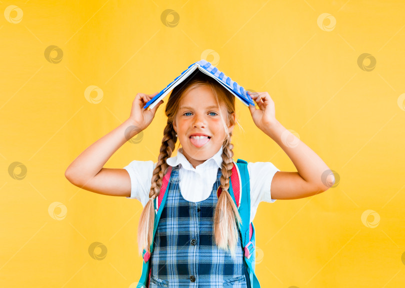 Скачать Счастливая маленькая школьница с книгой на голове, стоящая на желтом фоне. Концепция "Назад в школу" фотосток Ozero