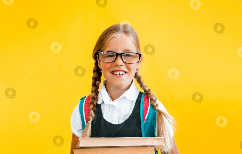 Скачать Портрет милой маленькой девочки на желтом фоне. Школьница смотрит в камеру, держа в руках книгу и поправляя очки. Концепция образования. фотосток Ozero