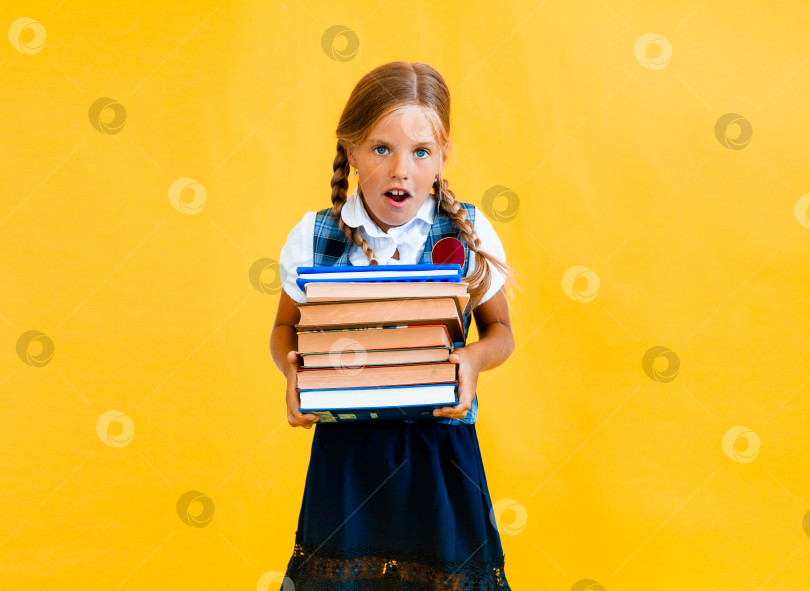 Скачать школьница с тяжелыми учебниками в руках на желтом фоне студии фотосток Ozero