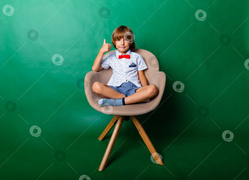 Скачать Счастливый мальчик сидит на стуле и показывает класс. Концепция образования и школы фотосток Ozero