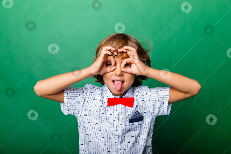 Скачать Веселый мальчик, держащий руки у лица в виде маски, выделенной на зеленом фоне фотосток Ozero