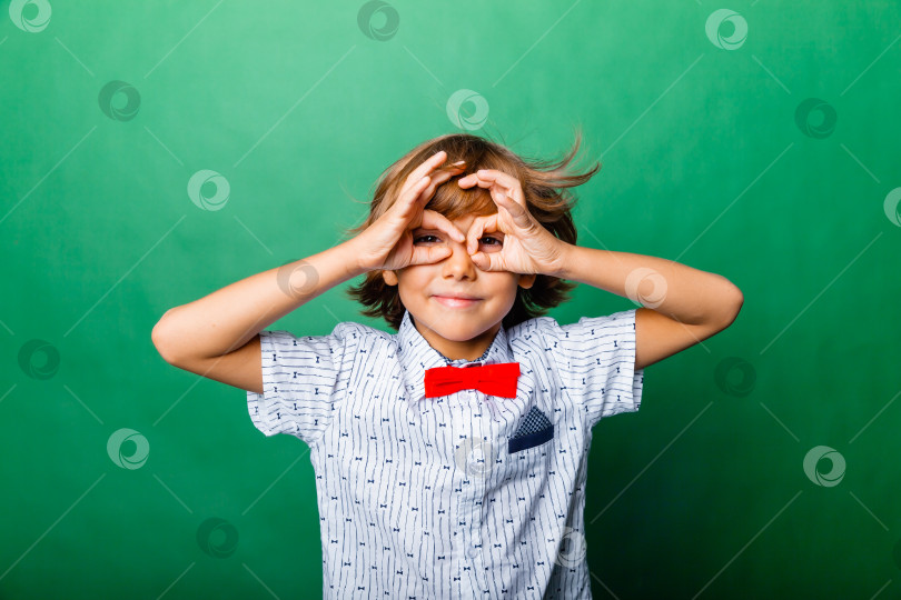Скачать Веселый мальчик, держащий руки у лица в виде маски, выделенной на зеленом фоне фотосток Ozero