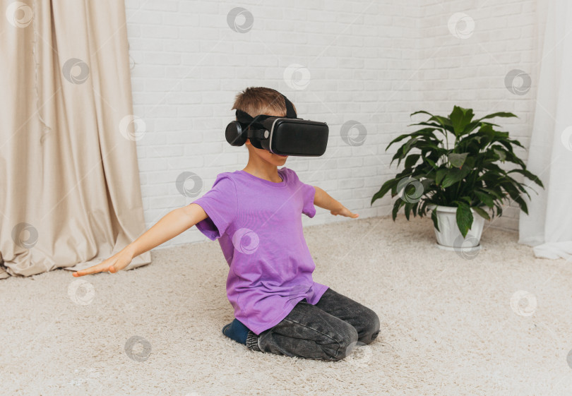 Скачать Взволнованный маленький мальчик в очках виртуальной реальности сидит на полу у себя дома. фотосток Ozero